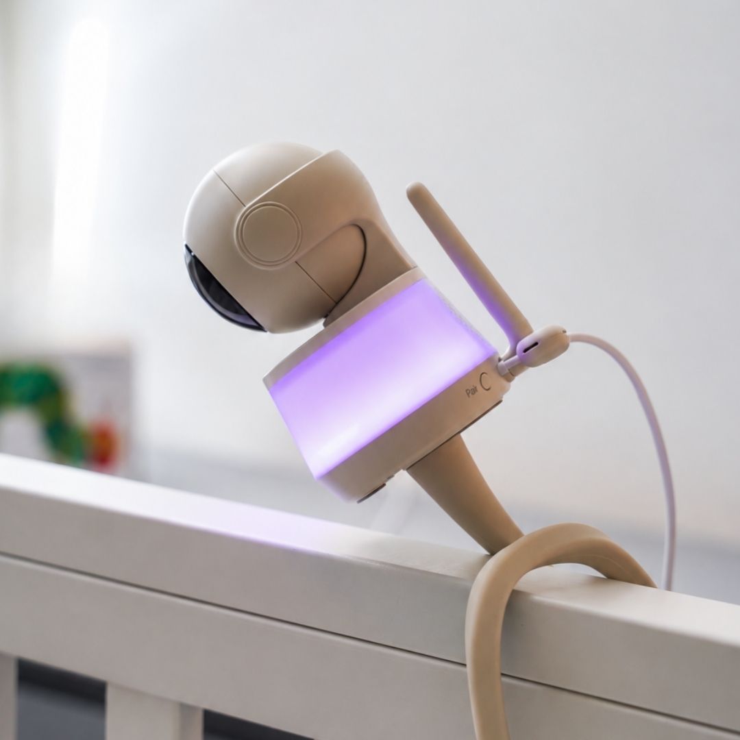 Luna Glow babyfoon camera met zacht paars nachtlampje op de rand van een babybedje